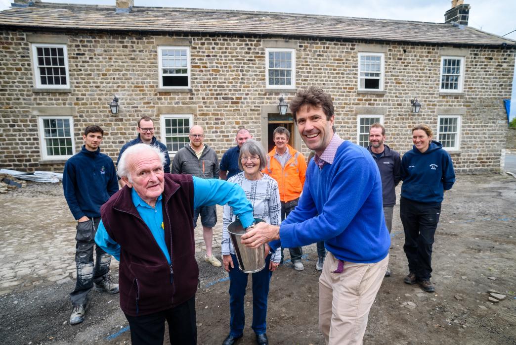 PUB WORK: Neil Turner picks the raffle winner with Sir Edward Milbank holding a champagne bucket full of names and Ann Orton, representing the parish church and village hall standing behind. Watching are some of the team working on the project